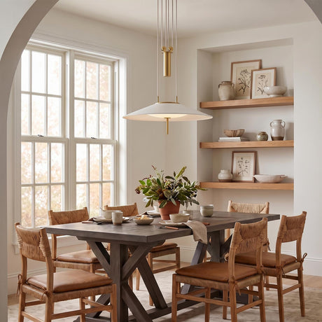 A contemporary dining room with the Elow Pull-Down LED Pendant 30 inch in matte white and aged brass hanging over a dark wood table and woven chairs.