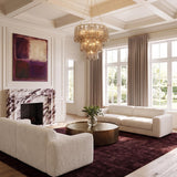 A contemporary living room featuring the Petronella Three-Tier Chandelier with smoke taupe swirled glass centered on a white coffered ceiling above white sofas and a marble fireplace.