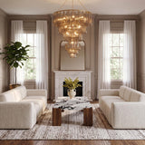 A transitional living room features the Petronella Four-Tier Chandelier with gold leaf and smoke taupe swirled glass above a marble coffee table flanked by cream sofas.