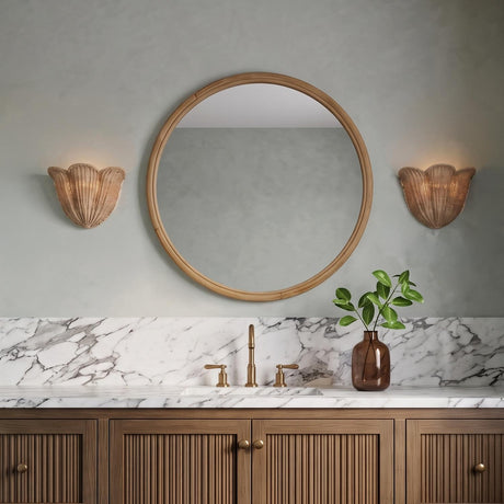 A coastal bathroom with two shell-shaped Candela Wall Sconce 10" fixtures in natural jute flanking a round wood mirror above a white marble vanity with brass faucets.