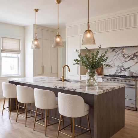 A transitional kitchen featuring three Bly Small Pendants in aged brass and smoke taupe glass over a marble island with bouclé stools and marble backsplash.