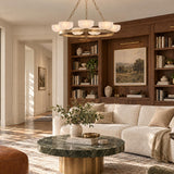 A transitional living room features the Halcyon 9 Light Chandelier 44", Patina Brass and Seeded Cloud Glass suspended above a green marble coffee table.