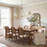 A transitional dining room with an aged brass linear pendant over a walnut table with six cane-back chairs and white paneled wainscoting.