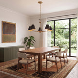 A transitional dining room with an aged brass and distressed bronze chandelier over a walnut table on a patterned rug beside a large window with greenery.