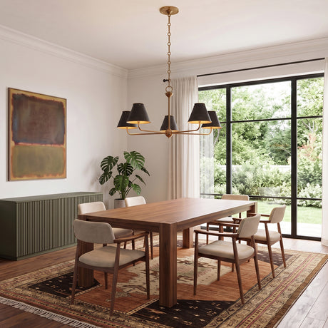 A transitional dining room with an aged brass and distressed bronze chandelier over a walnut table on a patterned rug beside a large window with greenery.