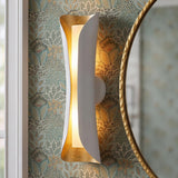 A transitional bathroom with the white and gold leaf Rhys Wall Sconce 21" mounted on botanical floral wallpaper beside a hammered gold round mirror.