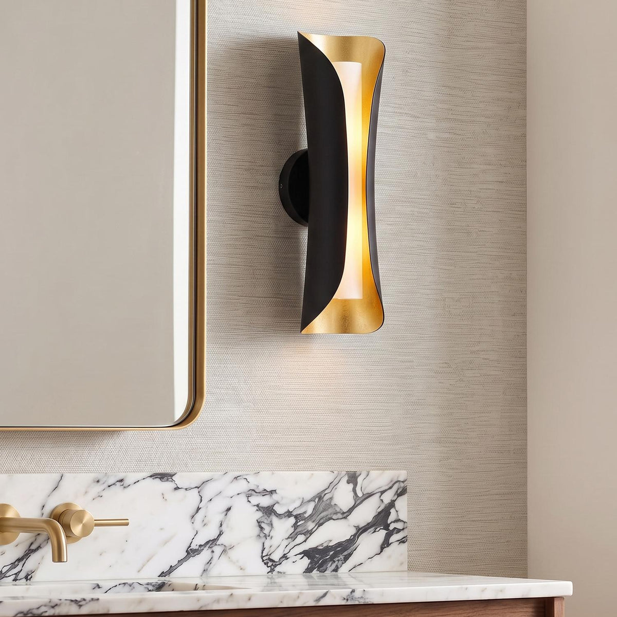 A contemporary bathroom featuring the Rhys Wall Sconce 21", Matte Black and Gold Leaf mounted beside a gold-framed mirror above a white marble vanity backsplash.