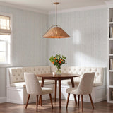 A coastal dining nook featuring the Gwenneth Large Pendant 25", Patina Brass and Rattan over a round walnut table with cream tufted banquette and striped wallpaper.