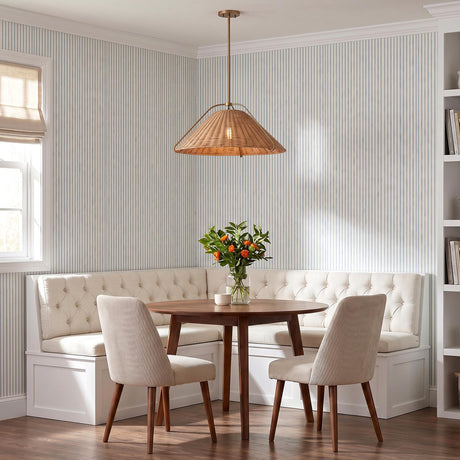 A coastal dining nook featuring the Gwenneth Large Pendant 25", Patina Brass and Rattan over a round walnut table with cream tufted banquette and striped wallpaper.