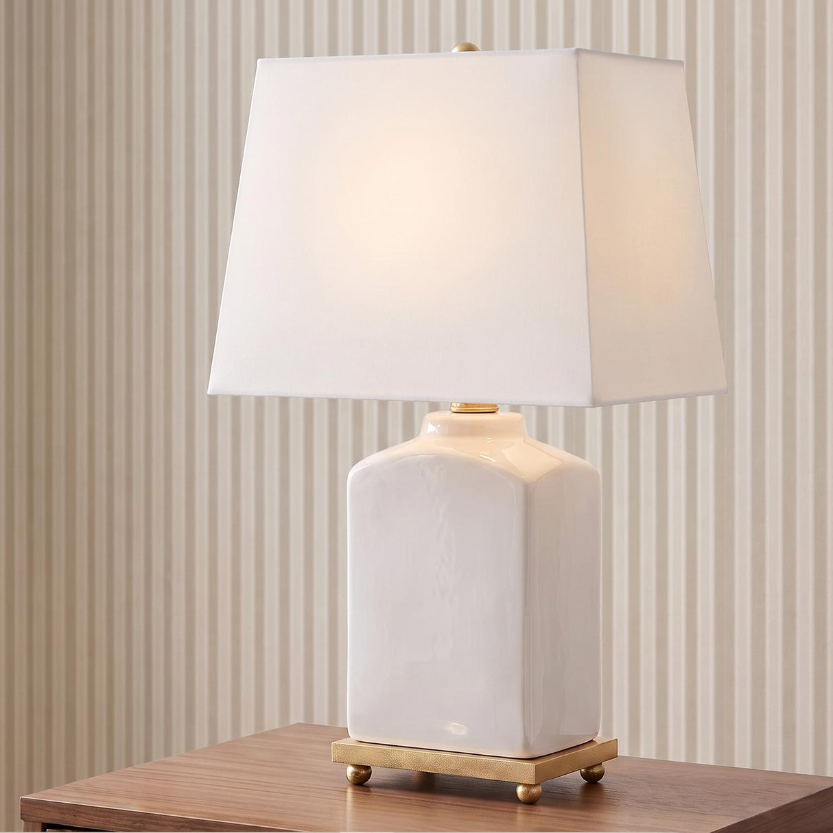 A transitional living room with the Hallie Table Lamp 17 inch, White Glaze with White Shade on a walnut side table against beige striped wallpaper.