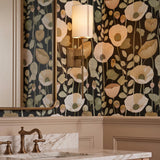 A traditional bathroom with a patina brass wall sconce featuring a linen shade mounted on floral wallpaper beside a brass-framed mirror and white marble vanity.
