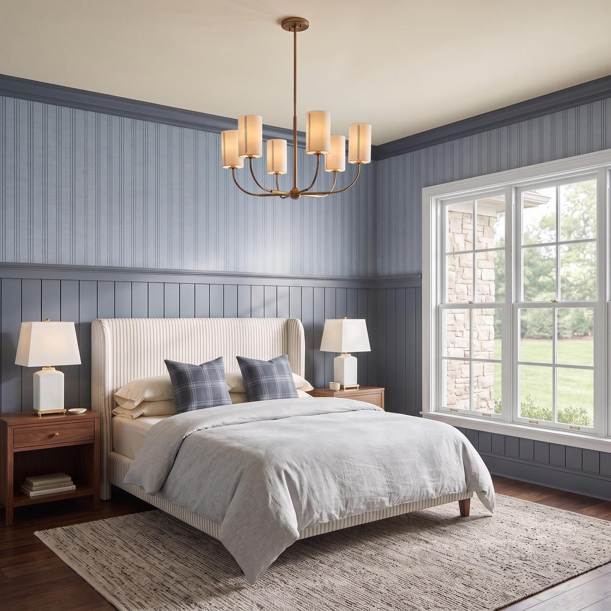 A traditional bedroom with the Hansel Chandelier 30", Patina Brass featuring linen shades hung over a striped headboard bed and blue wainscoting walls.
