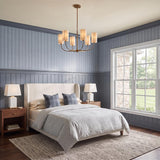 A traditional bedroom with the Hansel Chandelier 30", Patina Brass featuring linen shades hung over a striped headboard bed and blue wainscoting walls.