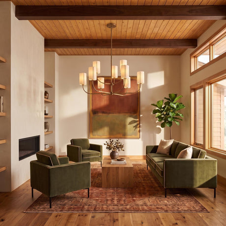A mid-century living room featuring the Hansel Two-Tier Chandelier in patina brass with linen shades suspended from a beamed wood ceiling over olive green velvet furniture.