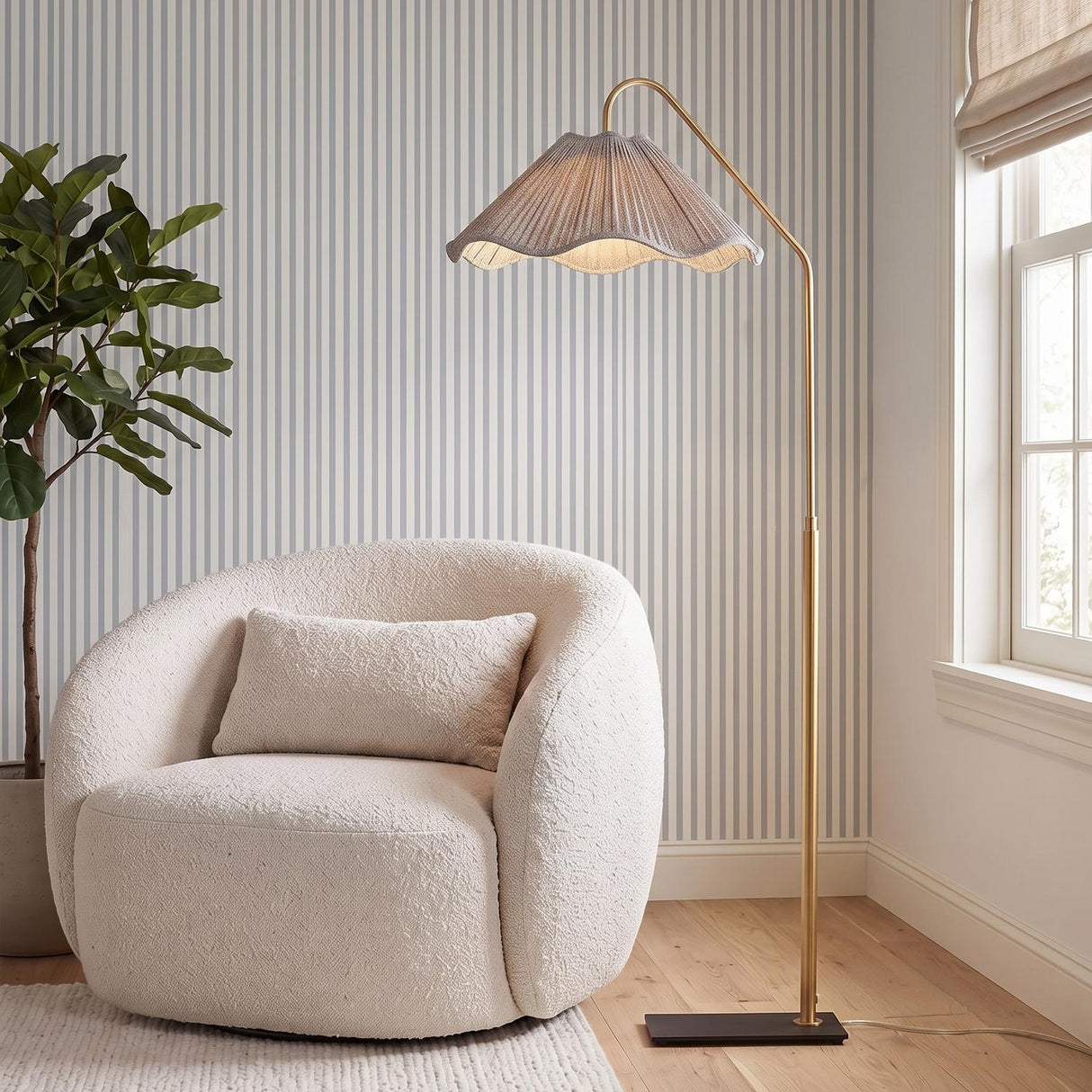 A contemporary living room featuring the Fiona Floor Lamp 60" in aged brass beside a white boucle chair, set against striped wallpaper and light wood floors.