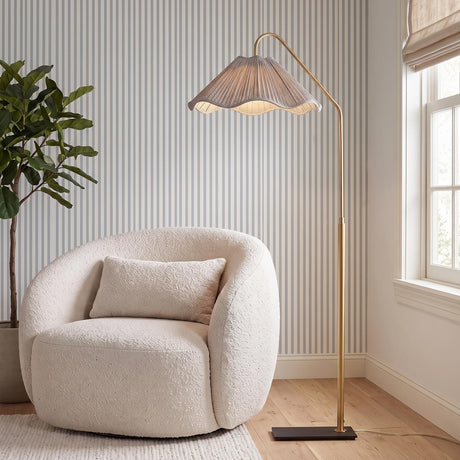 A contemporary living room featuring the Fiona Floor Lamp 60" in aged brass beside a white boucle chair, set against striped wallpaper and light wood floors.