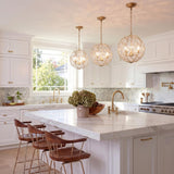 A transitional kitchen with three soft brass globe pendants featuring glass leaf accents hanging over a white marble island with dark wood bar stools.