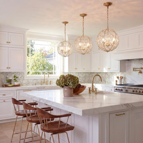 A transitional kitchen with three soft brass globe pendants featuring glass leaf accents hanging over a white marble island with dark wood bar stools.