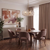 A contemporary dining room featuring the Esme Chandelier in soft brass and clear glass suspended over a round walnut table with mauve velvet chairs and herringbone floors.