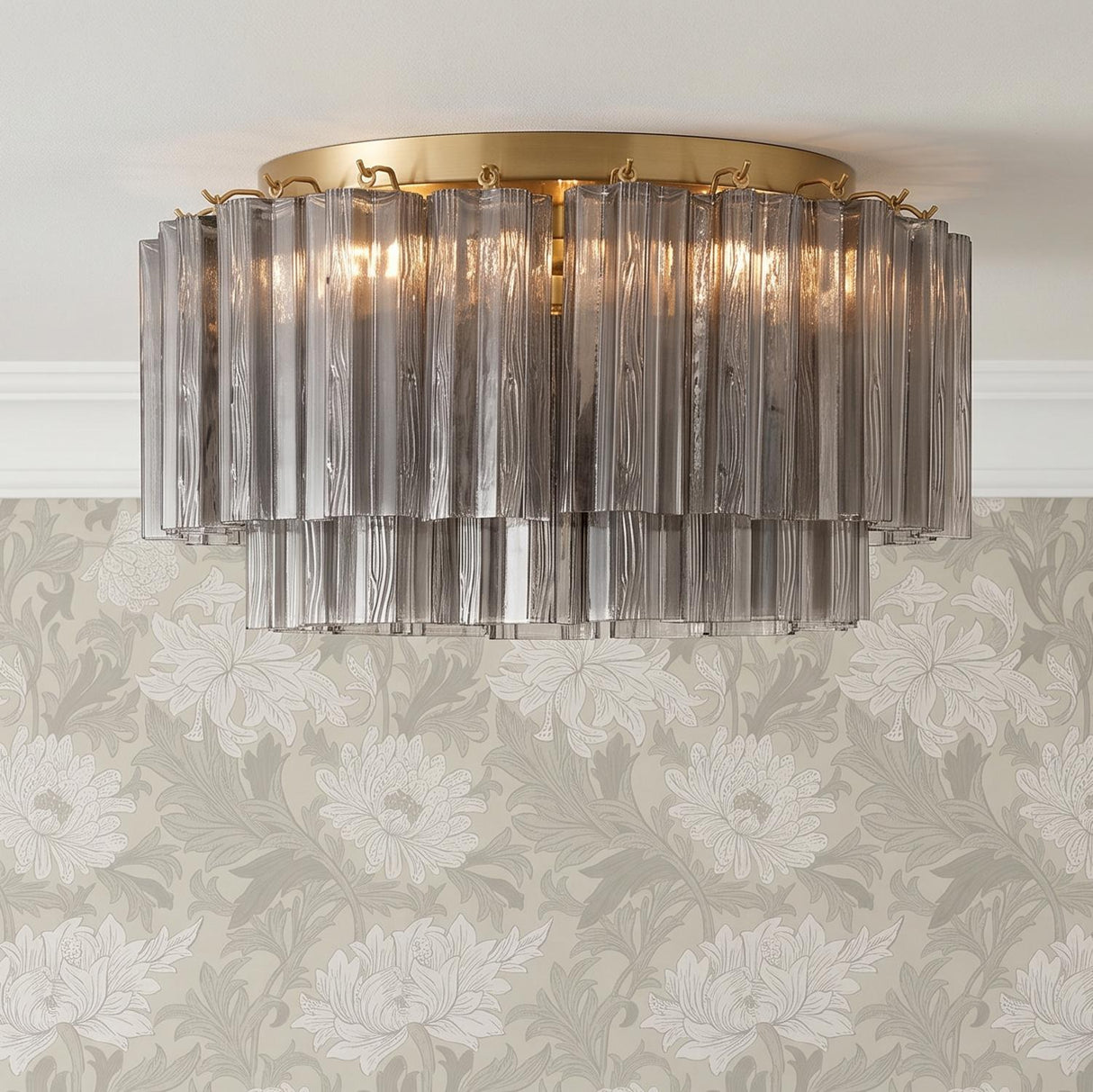 A transitional foyer featuring the Grace Flush Mount 22", Brass with Smoke Glass mounted on the ceiling against beige floral wallpaper and white crown molding.