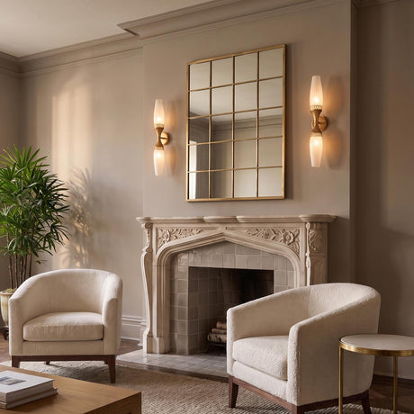 A transitional living room featuring Amarael wall sconces in gold leaf and cloud glass flanking a grid mirror above a carved stone fireplace mantle and textured ivory armchairs.