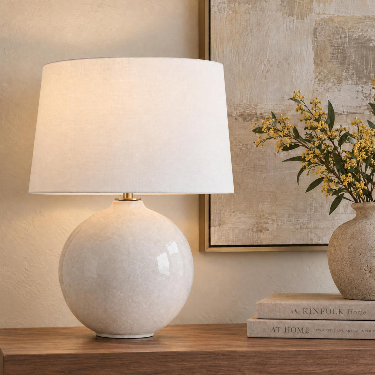 A transitional living room setting featuring the Syrene Table Lamp 21", Glossy Chalk with White Shade resting on a wood console alongside stacked books and yellow flowers.