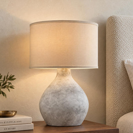 A transitional bedroom featuring the Helios Table Lamp 27", Gray Cloud with Natural Linen Shade set on a wooden nightstand beside a textured bouclé headboard.
