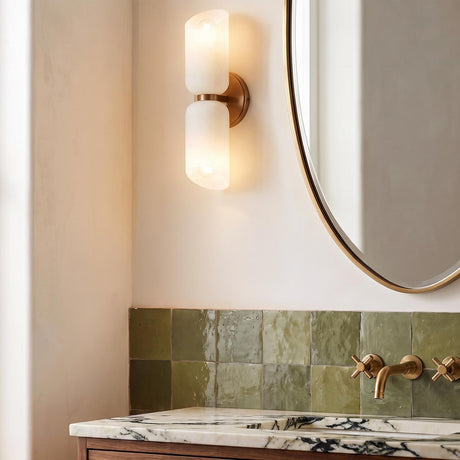 A contemporary bathroom with the Vivara 2 Light Wall Sconce in patina brass and cloud glass mounted beside an oval mirror over green textured tiles.