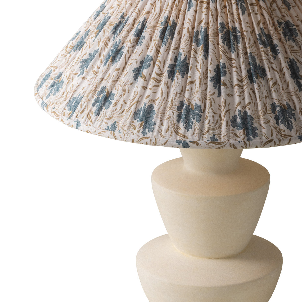 A close-up of a Bonnie Table Lamp with a pleated fabric shade featuring a blue floral and gold vine pattern on a cream background, paired with a matte cream-colored ceramic base.
