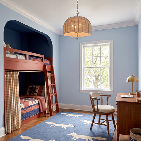 A traditional bedroom with a gold leaf and natural rope drum pendant hanging over a blue fox-print rug, wooden desk, and red bunk beds.