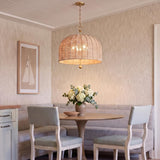 A coastal dining room features a gold leaf and natural rope pendant hanging above a round wooden table surrounded by a light gray banquette.