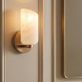 A transitional bathroom featuring the Vivara Wall Sconce with patina brass and cloud glass mounted on a paneled beige wall beside a matching brass-framed mirror.