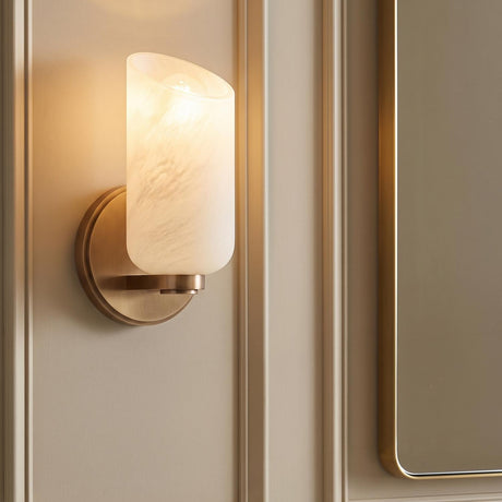 A transitional bathroom featuring the Vivara Wall Sconce with patina brass and cloud glass mounted on a paneled beige wall beside a matching brass-framed mirror.