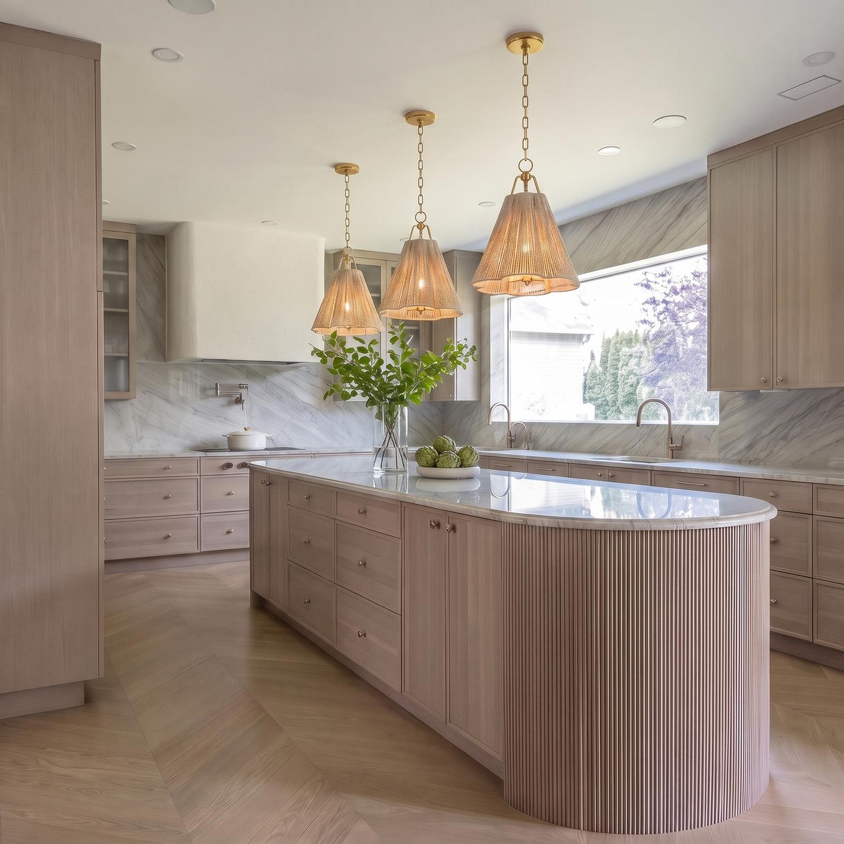A contemporary kitchen with three Birdie Medium Pendant 18" gold leaf and natural rope pendants hanging over a curved reeded island and marble countertops.
