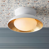 A transitional foyer with a white and gold leaf flush mount featuring a frosted glass globe on a blue floral wallpapered ceiling above blue wall paneling.