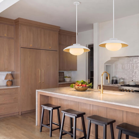 A contemporary kitchen with two Vera Large Pendants in white and gold leaf hanging over a white marble island with light wood cabinetry and black stools.