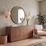 A transitional bedroom featuring the Basil Wall Sconce 19", Aged Brass with Red Primrose Printed Shade flanking a large round mirror above a nine-drawer walnut dresser.