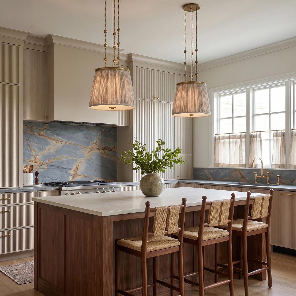 A transitional kitchen with two Wilma Medium Pendants in aged brass and taupe print over a quartz island featuring walnut barstools and blue marble backsplash.