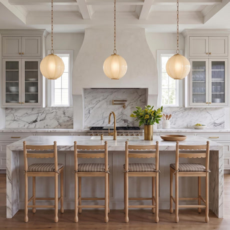 A modern farmhouse kitchen with three Livia Medium Pendants in aged brass and buttermilk glass over a marble waterfall island under a white coffered ceiling.