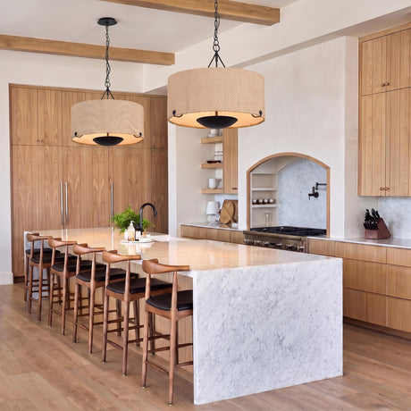 A transitional kitchen features two Linwood Extra Large Pendants in forged iron and raffia over a white marble waterfall island with wood beams and matching cabinets.