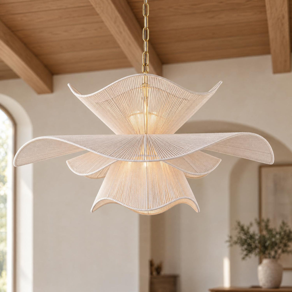 A transitional living room featuring the Lotus Chandelier 34", Aged Brass and Natural Cotton suspended from an exposed wood beamed ceiling above neutral plaster walls.