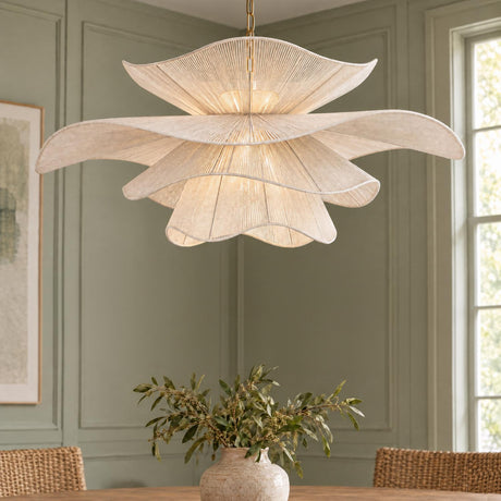 A transitional dining room featuring the Lotus Chandelier 44", Aged Brass and Natural Cotton suspended over a wood dining table flanked by woven chairs against green paneled walls.