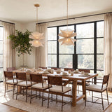 A transitional dining room with two Lotus Pendant 20-inch Aged Brass and Natural Cotton fixtures hanging over a wood table with woven leather chairs and large windows.