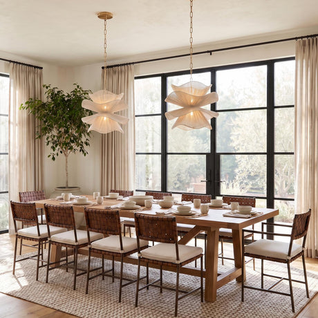 A transitional dining room with two Lotus Pendant 20-inch Aged Brass and Natural Cotton fixtures hanging over a wood table with woven leather chairs and large windows.
