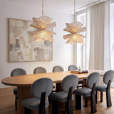 A modern dining room featuring two Lotus Pendants in aged brass and natural cotton suspended over a light wood oval table beside a large abstract painting.