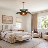 A transitional bedroom with the Lotus Chandelier 44", Patina Brass and Rosemary Cotton hanging from a standard ceiling over a striped upholstered bed and cream bouclé chairs.