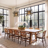 A contemporary dining room featuring two Lotus Pendants in patina brass and rosemary cotton hanging over a long wood table with woven cane chairs.
