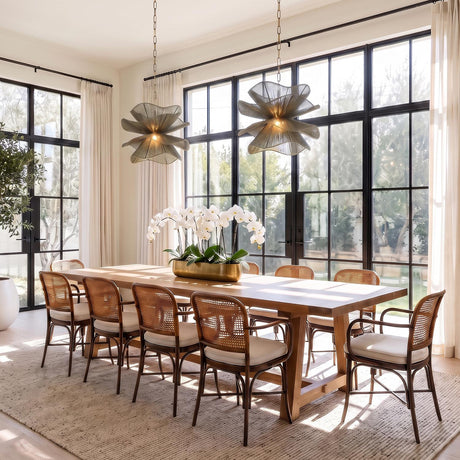 A contemporary dining room featuring two Lotus Pendants in patina brass and rosemary cotton hanging over a long wood table with woven cane chairs.