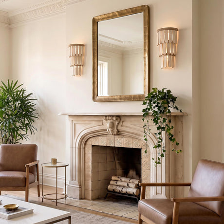 A traditional living room with two Hannigan Wall Sconce 18-inch fixtures in whitewash wood and patina brass flanking a gold mirror above a carved stone fireplace.