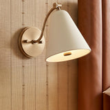 A transitional bedroom with a patina brass and soft sand Bryden Pivot Wall Sconce mounted on striped beige wallpaper beside a brown leather headboard.
